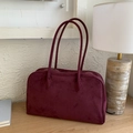 Detail view of burgundy suede tote bag with silver zipper on a wooden table setup - Red