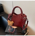 Dettaglio della borsa a secchiello lucida bordeaux con ciondolo a orso e motivi in pelle - Rosso Vino Con Pendente
