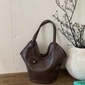 Artistic close-up of a vintage dark brown faux leather tote bag with a gold buckle pendant - Brown