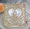 Close-up of laser-cut gold glitter wedding invitation with heart and couple silhouette - Rose Gold