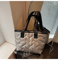 Close-up of silver quilted tote bag with V-pattern texture and black woven handles - Gold