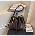 Detail view of brown pleated bucket bag with decorative wooden beads on a blue stool - With Charm / Brown