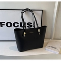 Detalle de bolso tote negro con herrajes dorados y logotipo sobre textura de cuero - Negro