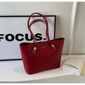 Detalle de bolso tote rojo de cuero con asas largas y hebillas doradas en ambiente minimalista - Rojo
