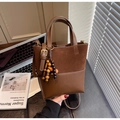 Détail du sac seau en daim marron mat avec pompon perlé et logo embossé sur le cuir - Avec Pendentif / Marron