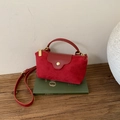 Detalle del mini bolso de ante rojo sobre libro verde con cremallera dorada y correa - Gamuza Sintética Rojo