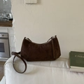 Detail der dunkelbraunen Wildleder-Halbmondtasche mit Silberbeschlägen auf weißem Sofa - Braun