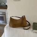 Detailansicht einer braunen Wildleder-Hobo-Tasche auf einem Sofa mit Silberbeschlag - Braun