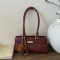 Detailaufnahme einer weinroten Vintage-Tasche mit goldenem Verschluss und Bärenanhänger - Rot mit Anhänger
