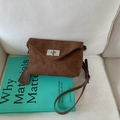 Minimalist dark brown frosted leather crossbody bag with silver rotating lock on white sofa - Brown
