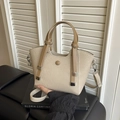 Beige woven bucket bag with camel leather handles on a decorative book and black sofa - Off White