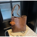 Braune Beuteltasche aus Leder mit Plüschbär-Anhänger und Kontrastseil auf Steinfläche - Braun mit Anhänger