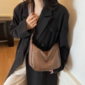 Sac hobo marron café en cuir porté à l'épaule par un mannequin en veste noire - Marron