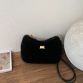 Elegante bolso bandolera de felpa negra con logo dorado sobre superficie de madera - Negro