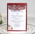 Macro detail of laser-cut burgundy wedding invitation sleeve with floral inner card - Dark Red