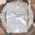 Detail of silver glitter laser cut wedding invitation with white satin bow on a plate - Silver Glitter