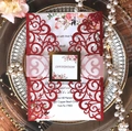 Close-up of laser-cut red wedding invitation with floral insert and glittery gold band - Glitter Red