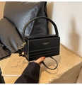 Detalle de bolso caja de cuero negro con letras doradas sobre soporte de piedra minimalista - Negro