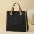 Detailed close-up of a black canvas tote bag with khaki contrast handles and metal button pocket - Black
