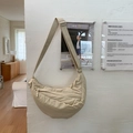 Dettaglio della borsa a tracolla a mezzaluna in nylon kaki su una parete minimalista - Bianco Sporco
