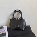 Close-up of black glossy shell handbag featuring decorative bow and silver hardware detail - Black