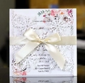 Elegant white laser cut snowflake wedding invitation with a cream satin bow on dark mirror - White