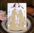 Close-up of laser-cut wedding card featuring floral print and couple silhouette on a vintage tray - Beige Gold