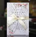Detail of laser-cut wedding invitation featuring floral inner card and cream satin bow - White
