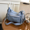 Blue denim crossbody bag with multiple zippers and wide strap on a table - Blue