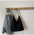 Detail einer schwarzen Wildleder-Shopper-Tasche mit Blumenanhänger an der Garderobe - Schwarz mit Anhänger