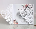 Close-up of laser-cut rose and heart lace patterns on a white wedding invitation card - White