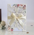 Detail of laser-cut wedding invitation with cream ribbon bow and floral inner card - White