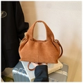 Detail of caramel suede cloud bag texture held in a hand over a travel setting - Brown