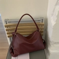 Borsa a tracolla in pelle bordeaux a grana litchi presentata su una sedia di legno - Rosso