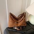 Sac bandoulière en daim marron caramel avec œillets argentés sur des livres - Marron