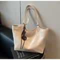 Detail of a beige leather tote bag with a decorative brown knot charm on art books - With Charm / Off White