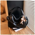 Dettaglio di borsa tote in pelle nera lucida con ciondolo a coniglio su tavolo in legno - Nero con ciondolo
