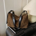 Leopard print tote bag with black leather straps and gold buckles on a leather sofa - Brown