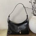 Detail of black wrinkled patent leather shoulder bag with gold zipper on a wooden table - Black