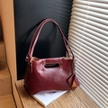 Vintage bordeauxrote Falten-Handtasche mit Bronze-Nieten auf einer Holzbank bei Licht - Burgunderrot