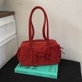 Detail der roten Wildledertasche mit Schleife und langem Griff auf grünem Buch - Rot