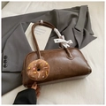 Detail of dark brown leather baguette bag with plush donut charm and bow on grey blazer - Brown