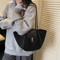 Chic black bucket tote bag in matte finish with gold buckle worn on shoulder - Black