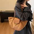 Brown leather bucket bag with gold clasp and dual strap, worn by a model in a cozy setting - Brown