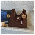 Detail of brown suede tote bag with metal M logo and plush bear charm on stone background - With Charm / Coffee