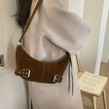 Detail of a brown suede crescent bag with silver buckles worn by a model in a cozy setting - Brown