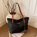 Large black tote bag with brown leather handles and decorative charm hanging - Black