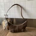 Brown suede crescent bag with vintage buckle straps on a minimalist wood surface - Brown