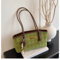 Detalle del bolso tote acolchado verde con asas marrones y colgante junto a un libro - Con Colgante / Verde