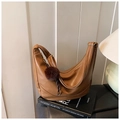 Close-up of brown leather dumpling bag with decorative plush ball and beaded charm - Brown